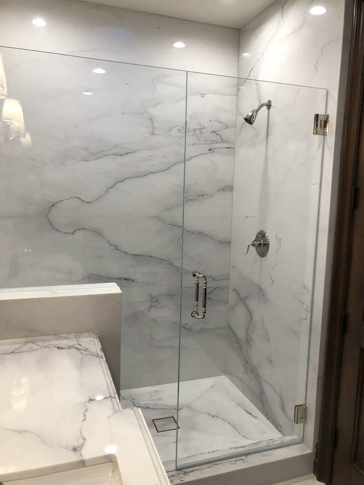 Frameless shower door and fixed panel in a marble-tiled bath
