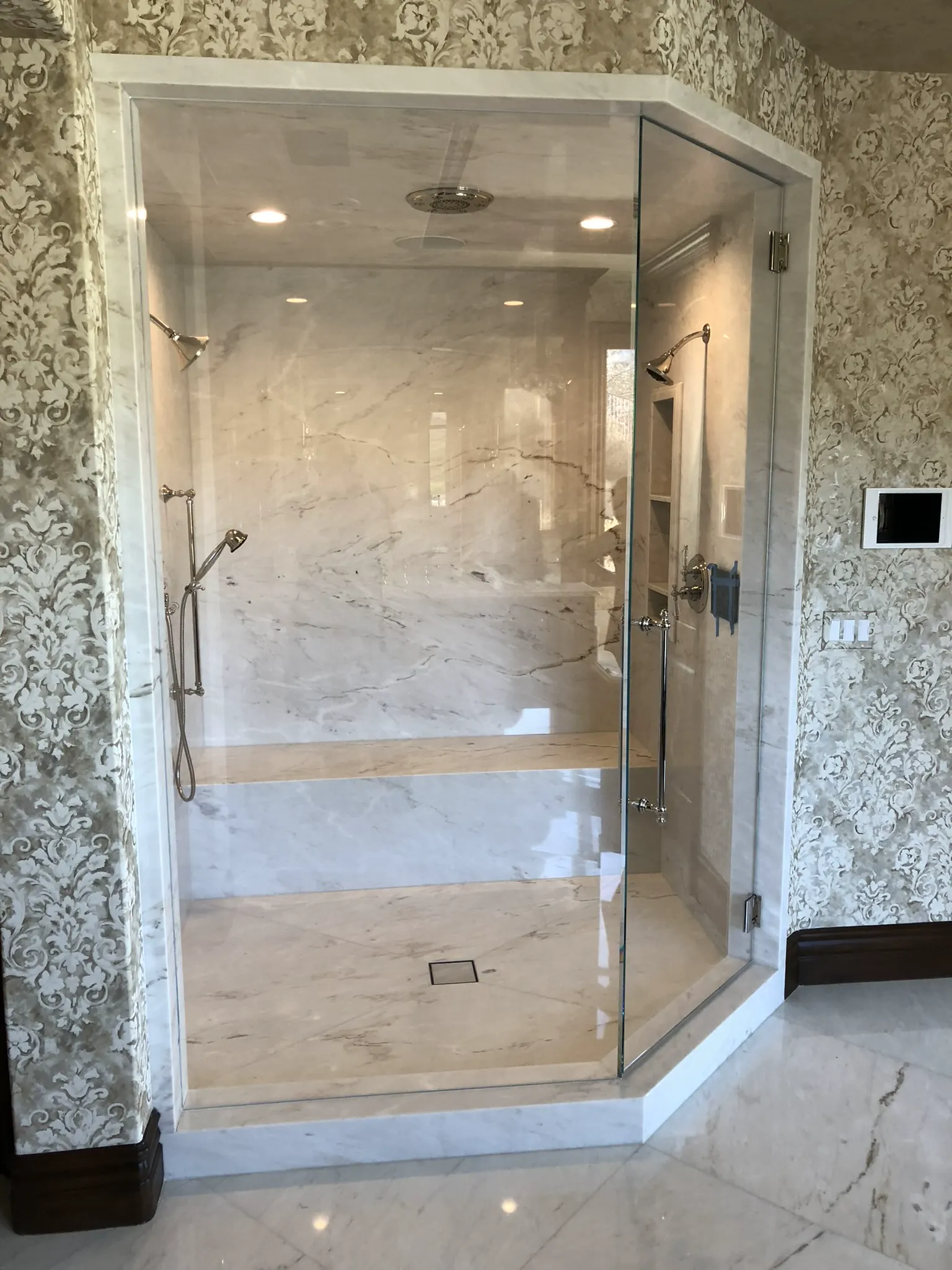 Frameless glass shower enclosure with patterned wallpaper and marble tile