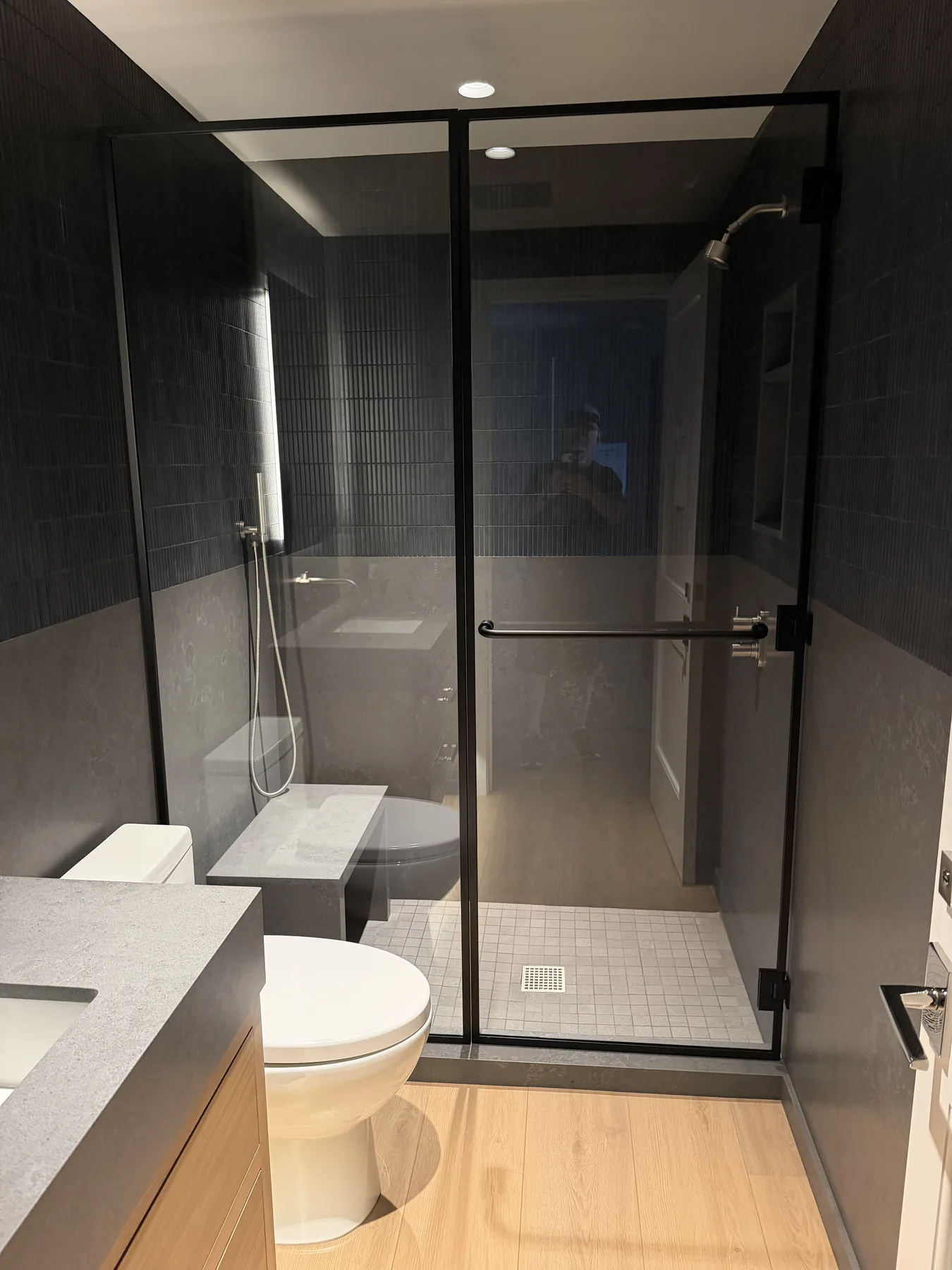 Black-framed glass shower door in a dark tiled bathroom